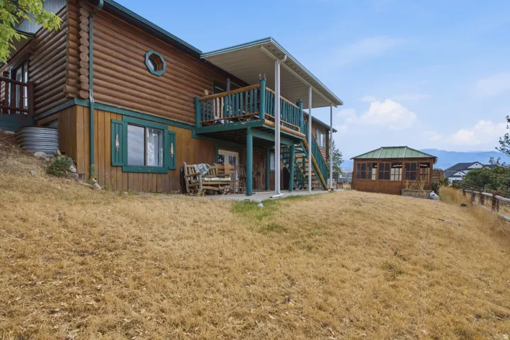 Log cabin exterior with an upper-level balcony, covered patio, and a separate wood-sided gazebo with a green roof