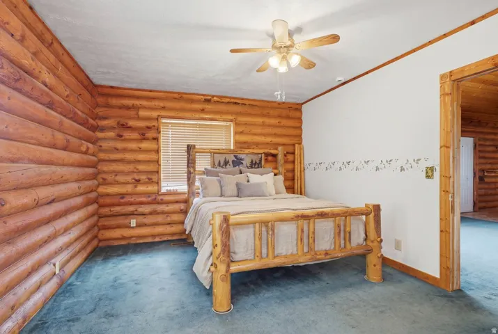 Log-paneled wall, white painted wall, ceiling fan, window with blinds, and blue carpeted flooring