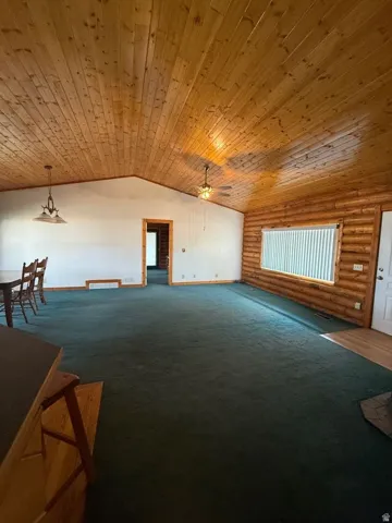 Spacious interior featuring a vaulted wood-paneled ceiling, exposed log wall, ceiling fan, and pendant lighting