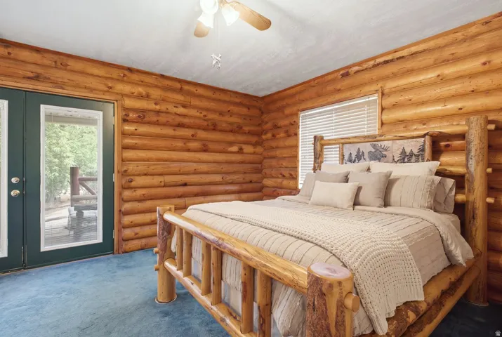Log wall paneling with a natural finish, ceiling fan, and direct outdoor access via glass-paned double doors