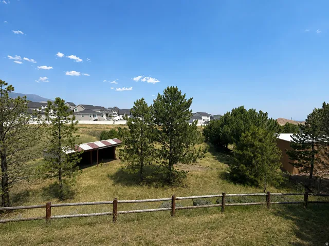 Expansive outdoor space featuring a rustic wooden fence, natural landscaping with mature trees, and a distant mountain range
