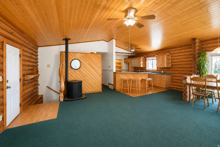 Open-concept living area featuring log walls, wood-finish flooring, and a wood stove