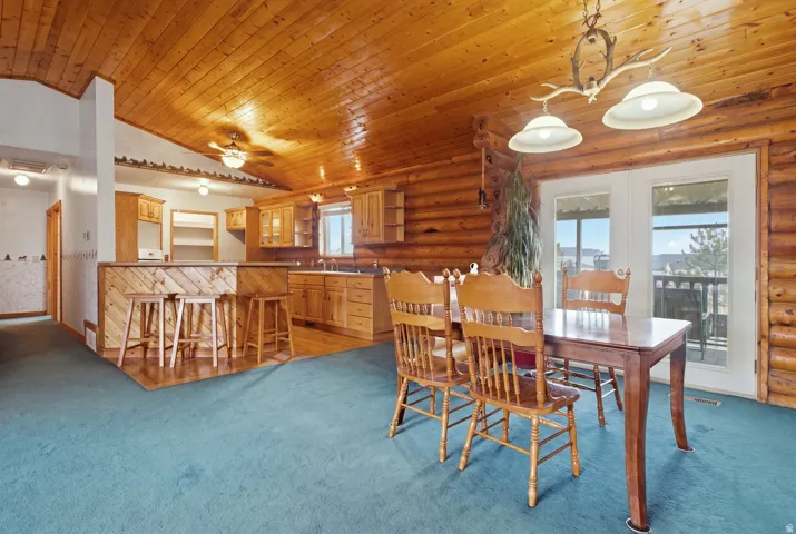 Vaulted wood-paneled ceiling with exposed beams, wood-plank walls, kitchen with wood cabinetry and built-in breakfast bar, and glass-paneled patio doors