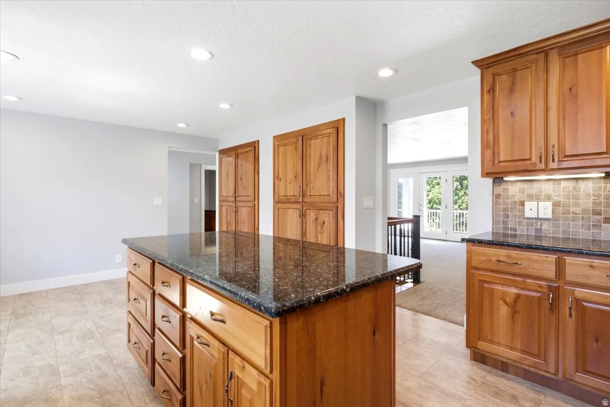 Kitchen island featuring a dark speckled countertop, warm wood cabinetry, and recessed lighting