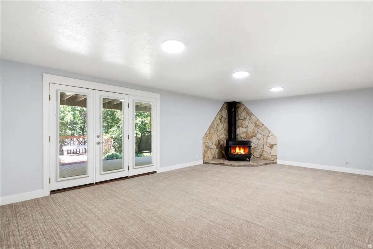 Spacious room featuring a stone-clad wood-burning stove, triple French doors, and recessed ceiling lighting