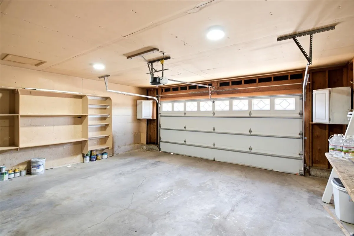 Spacious garage featuring a paneled garage door with decorative windows, concrete flooring, recessed lighting, built-in shelving, and exposed wood framing