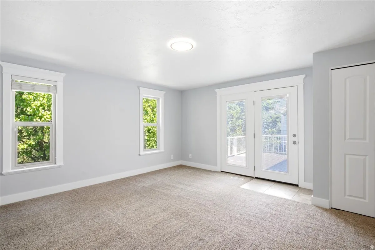 Neutral-toned carpeting extends throughout this room, complemented by two large windows with white trim and a double glass-panel door opening to a balcony with white railing