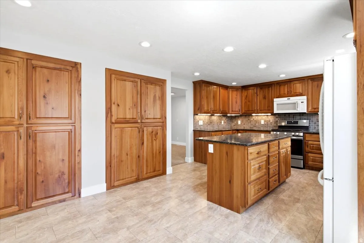 Kitchen featuring wood cabinetry, a center island with a dark countertop, stainless steel appliances, and a tiled backsplash