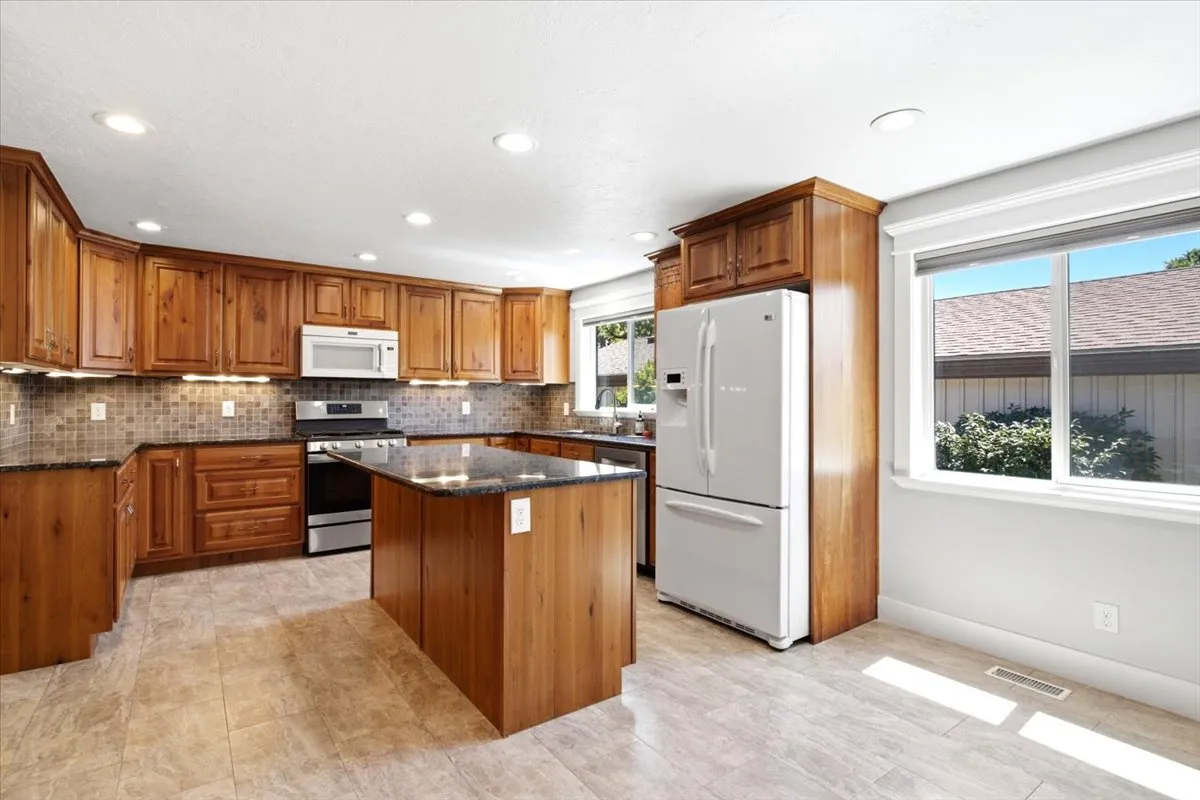 Kitchen featuring wood cabinetry, dark countertops, a tiled backsplash, a central island, and recessed lighting