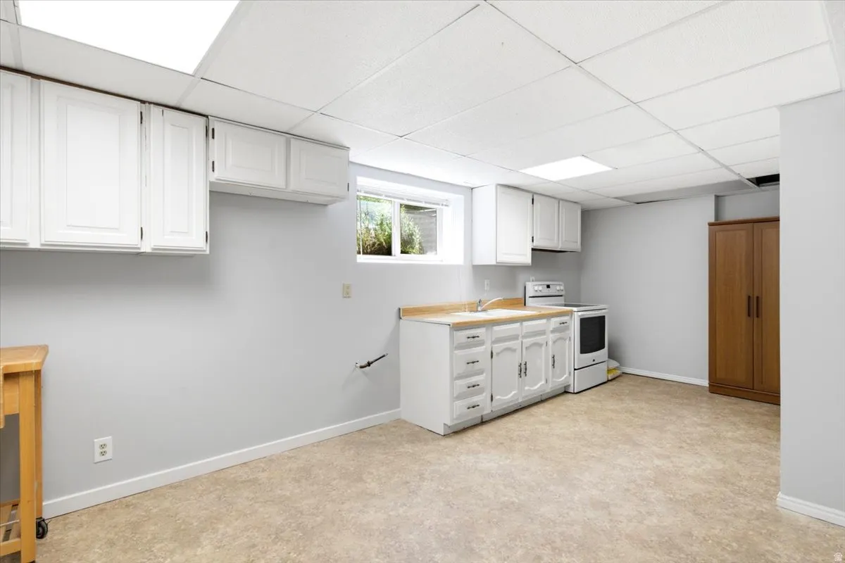 Lower-level space featuring a drop ceiling with integrated lighting, white cabinetry, laminate countertops, a stainless steel sink, and resilient flooring