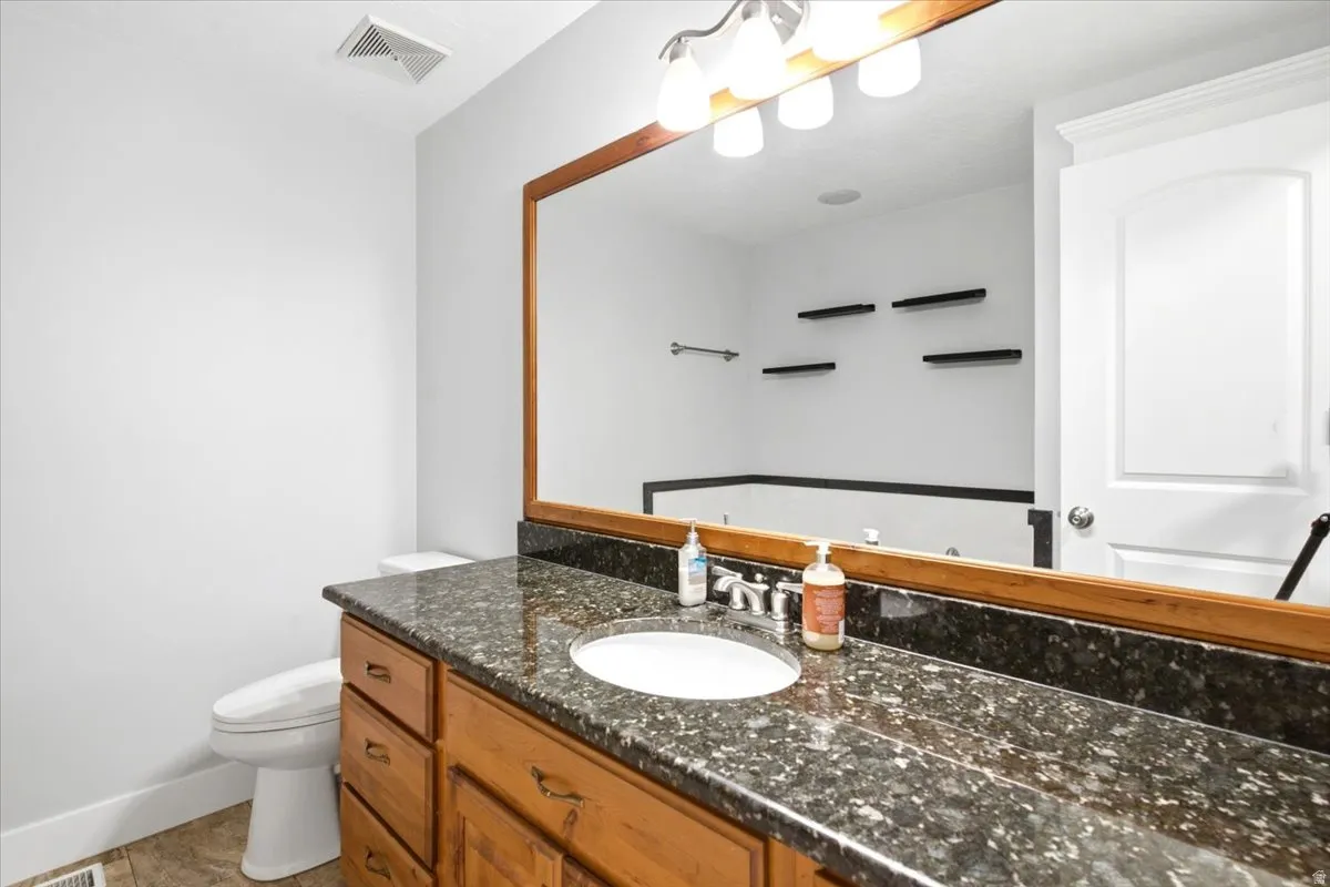 Bathroom featuring a wood-finish vanity with drawer storage, dark speckled countertop, and integrated sink