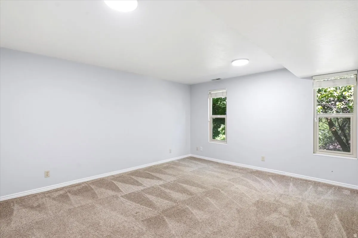 Spacious room featuring neutral carpeting, light blue walls, white trim, recessed lighting, and two windows with roller shades