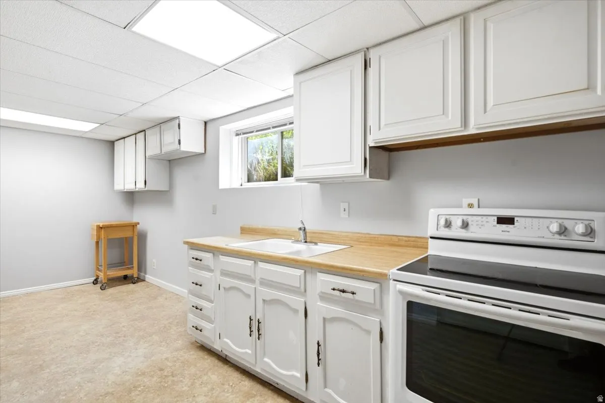 Functional kitchen area featuring white cabinetry, light wood-finish countertops, and a white electric range
