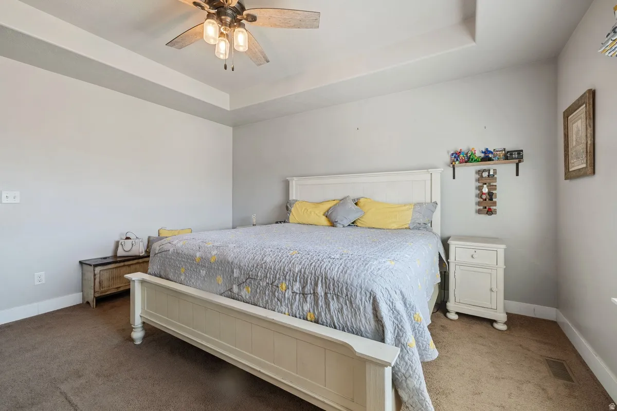 Spacious room featuring a tray ceiling with a ceiling fan, neutral wall paint, and brown carpet flooring