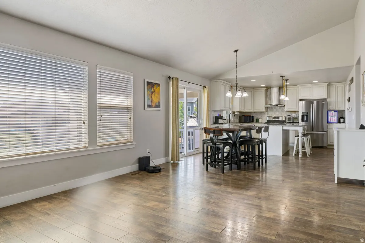 Open-concept living area featuring wood-finish flooring, vaulted ceilings, and large windows with blinds