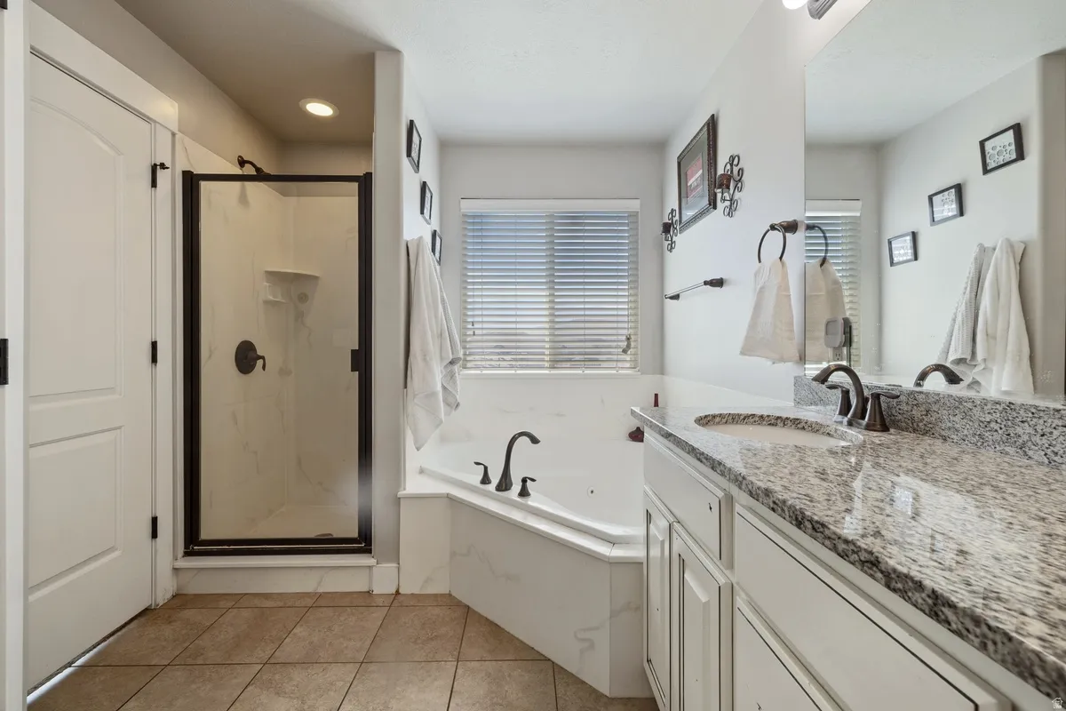 Bathroom featuring a corner soaking tub, separate shower with dark bronze fixtures, and a vanity with a stone countertop and integrated sink