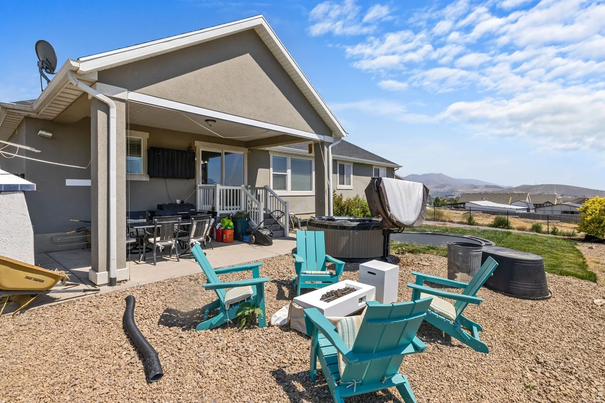 Expansive outdoor living area featuring a covered patio with dining space, a dedicated hot tub area, and a gravel-covered gathering space