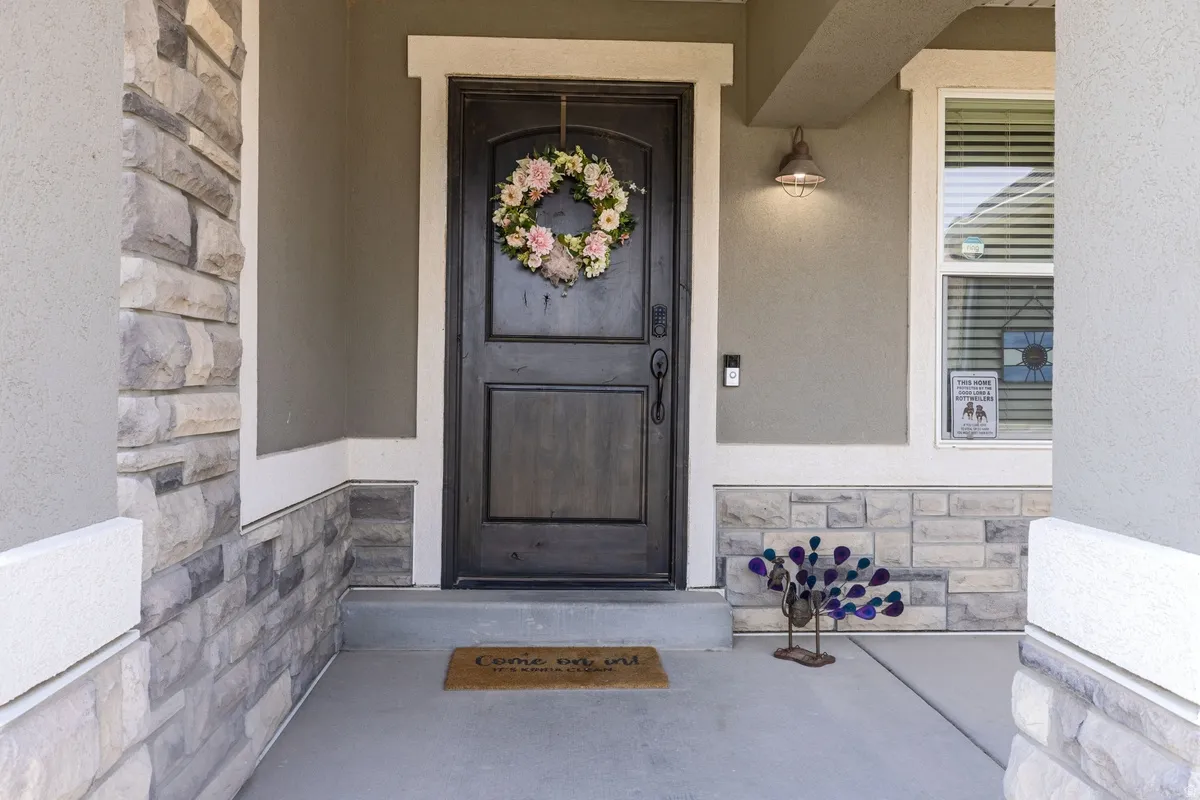 Inviting covered entryway featuring a dark wood-finish door with panel detailing, stone veneer accents, and a complementary exterior light fixture