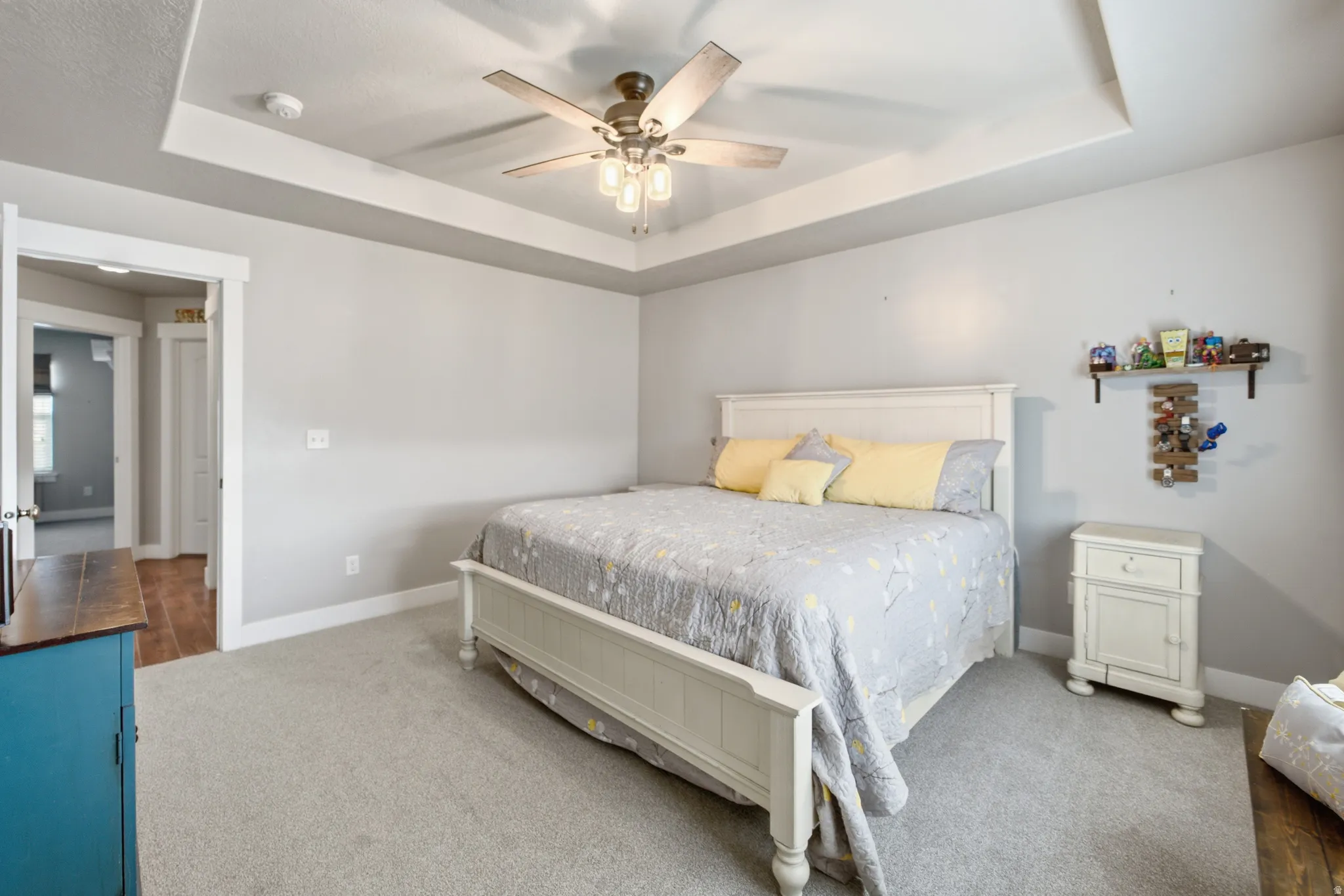 Tray ceiling with a decorative ceiling fan, light gray wall paint, and gray carpeting