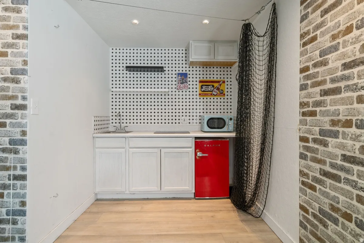 Compact kitchenette featuring white cabinetry, a light-toned countertop, and a white pegboard backsplash