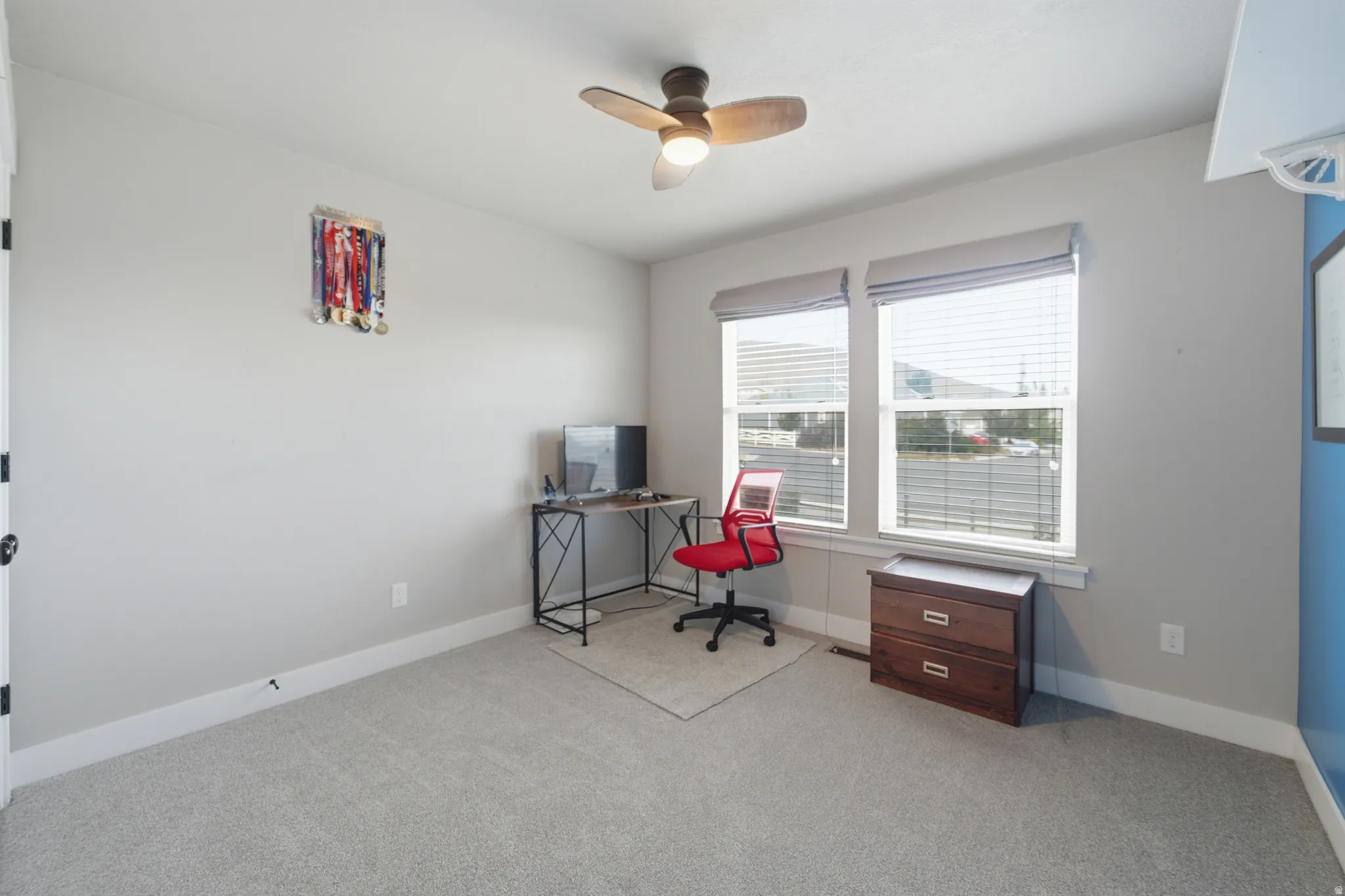 Carpeted room featuring a ceiling fan with integrated lighting, two windows with blinds, and light-toned walls
