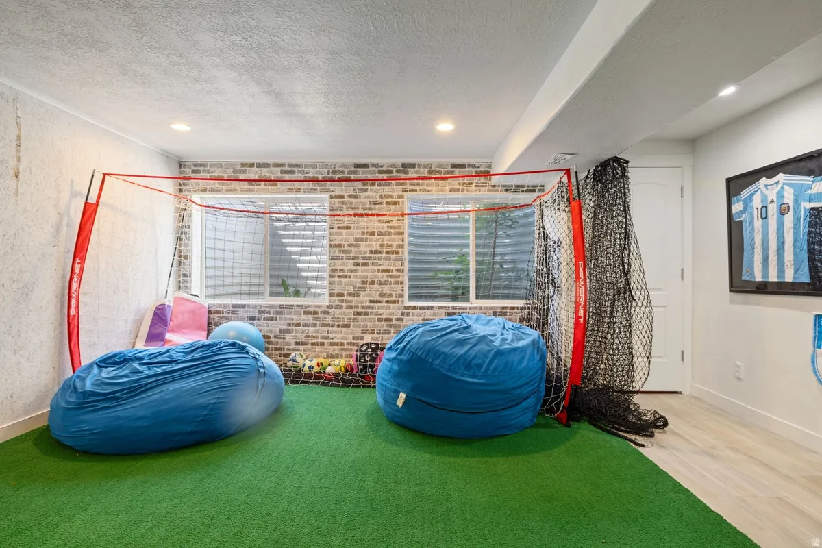 Recreational room featuring artificial turf flooring and a brick-pattern accent wall