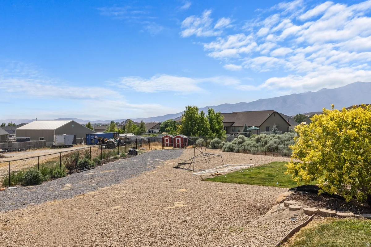 Expansive backyard featuring gravel and grass landscaping, a chain-link fence, and two red storage sheds