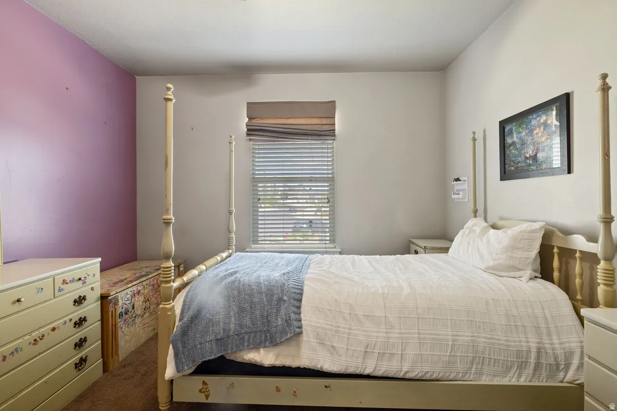 Bedroom featuring a window with blinds, a Roman shade, and carpet flooring
