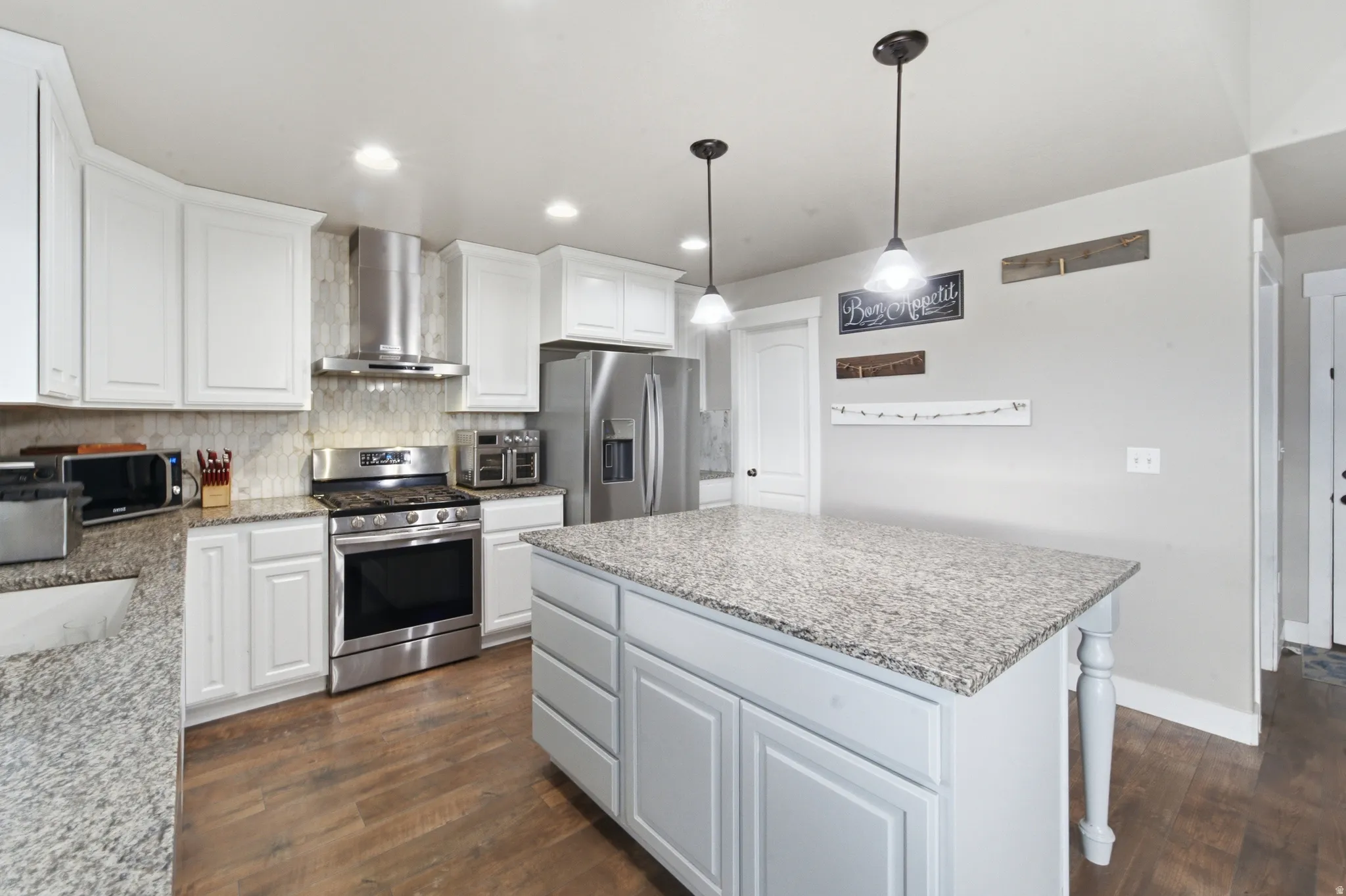 White cabinetry, granite countertops, stainless steel appliances, wood-finish flooring, and a kitchen island with pendant lighting