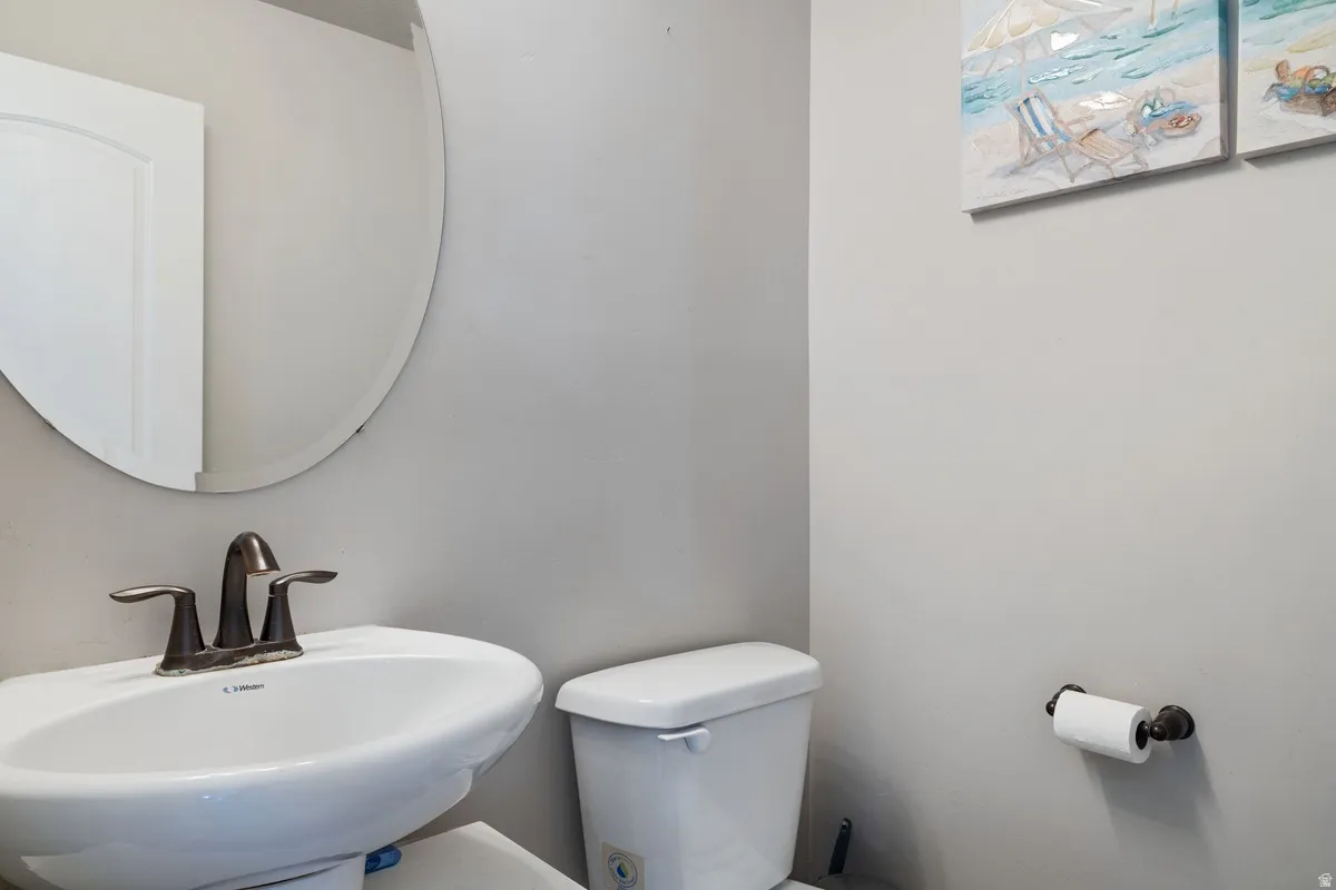 Pedestal sink with bronze-finish faucet, accompanied by a round frameless mirror and a white toilet
