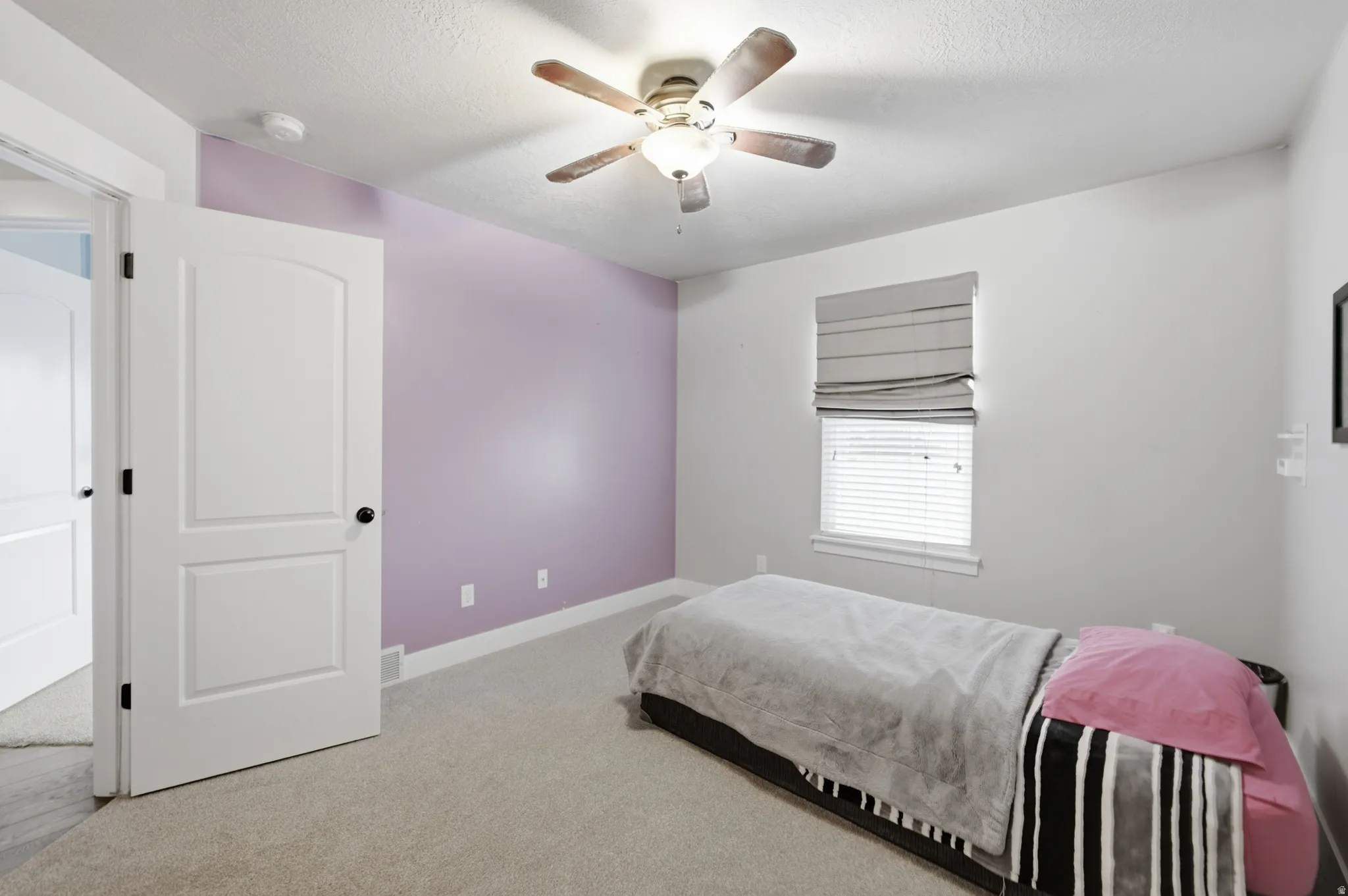 Light-toned carpeted flooring, a ceiling fan with light fixture, and a window with blinds