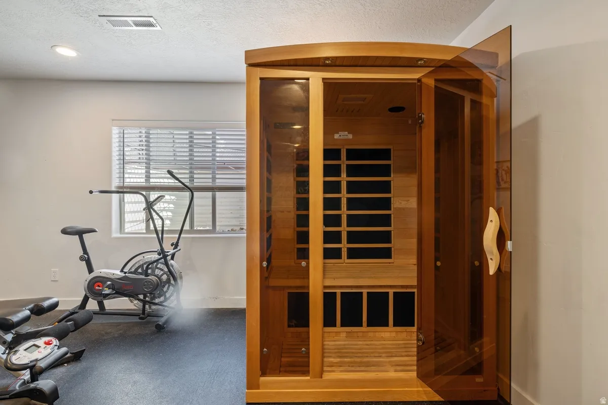 Dedicated fitness space featuring a built-in wood sauna with glass doors, recessed lighting, and a window with horizontal blinds