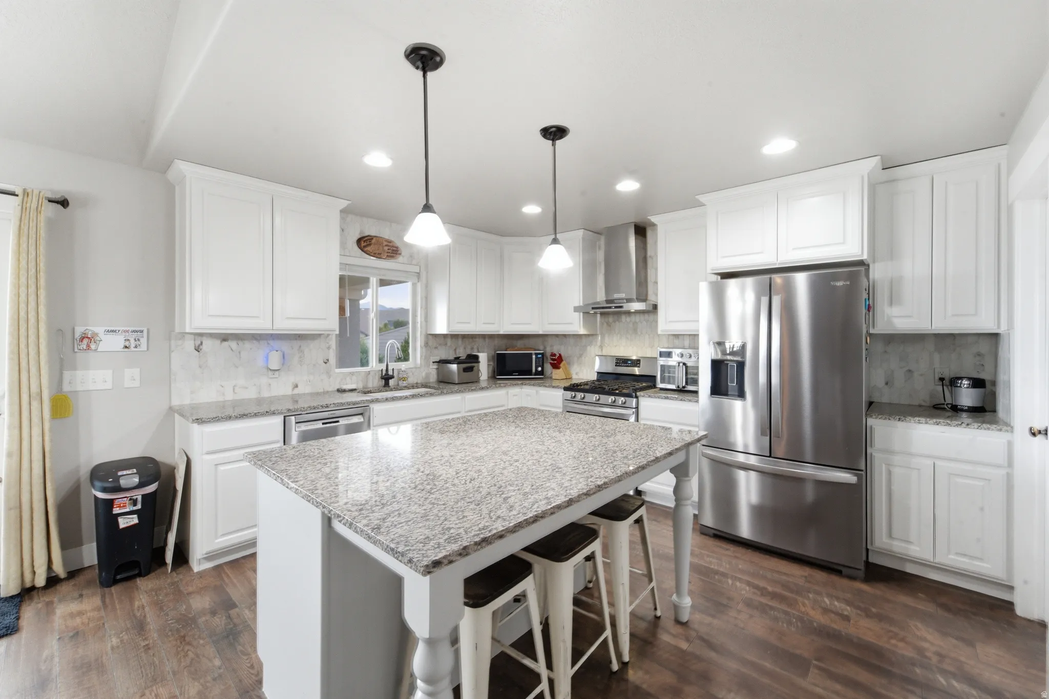 Kitchen featuring white cabinetry, wood-finish flooring, stainless steel appliances, granite countertops, and a center island with pendant lighting
