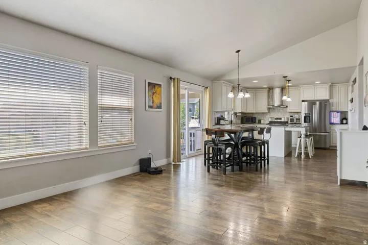 Open-concept living area featuring wood-finish flooring, vaulted ceilings, and large windows with blinds
