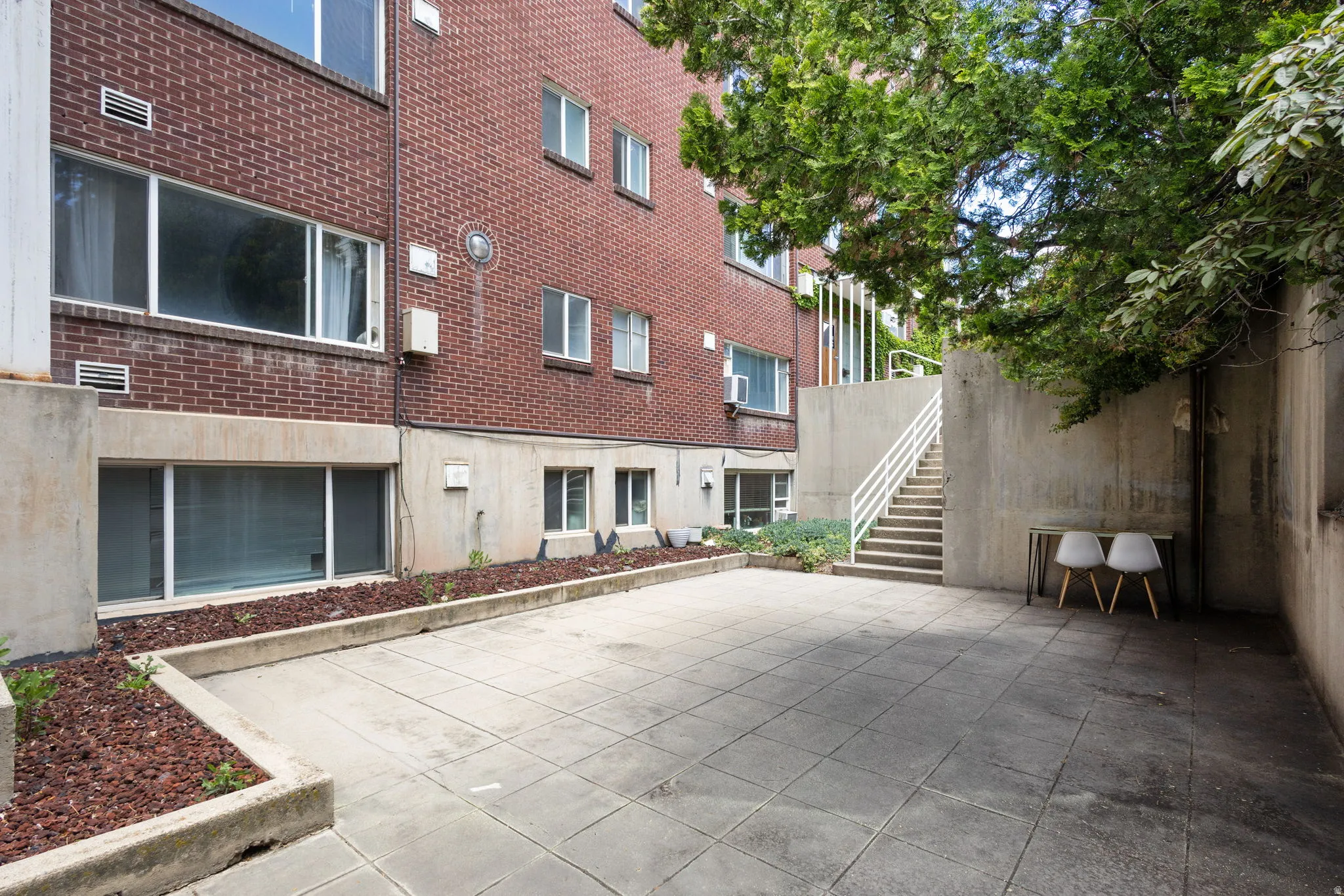 Expansive patio area featuring large concrete pavers, concrete retaining walls, and a brick exterior building