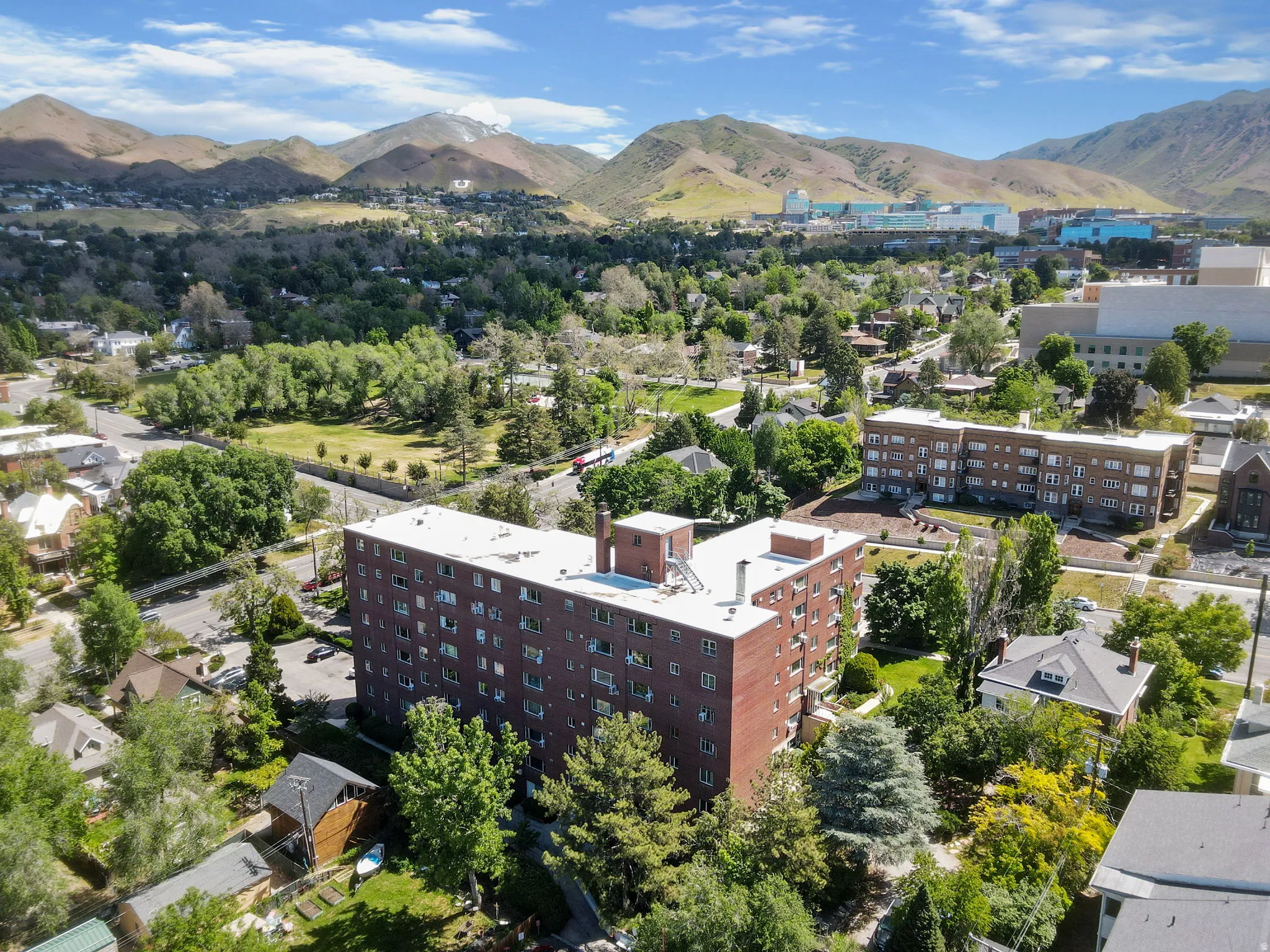 Multi-story brick building with multiple windows, surrounded by mature trees and paved areas