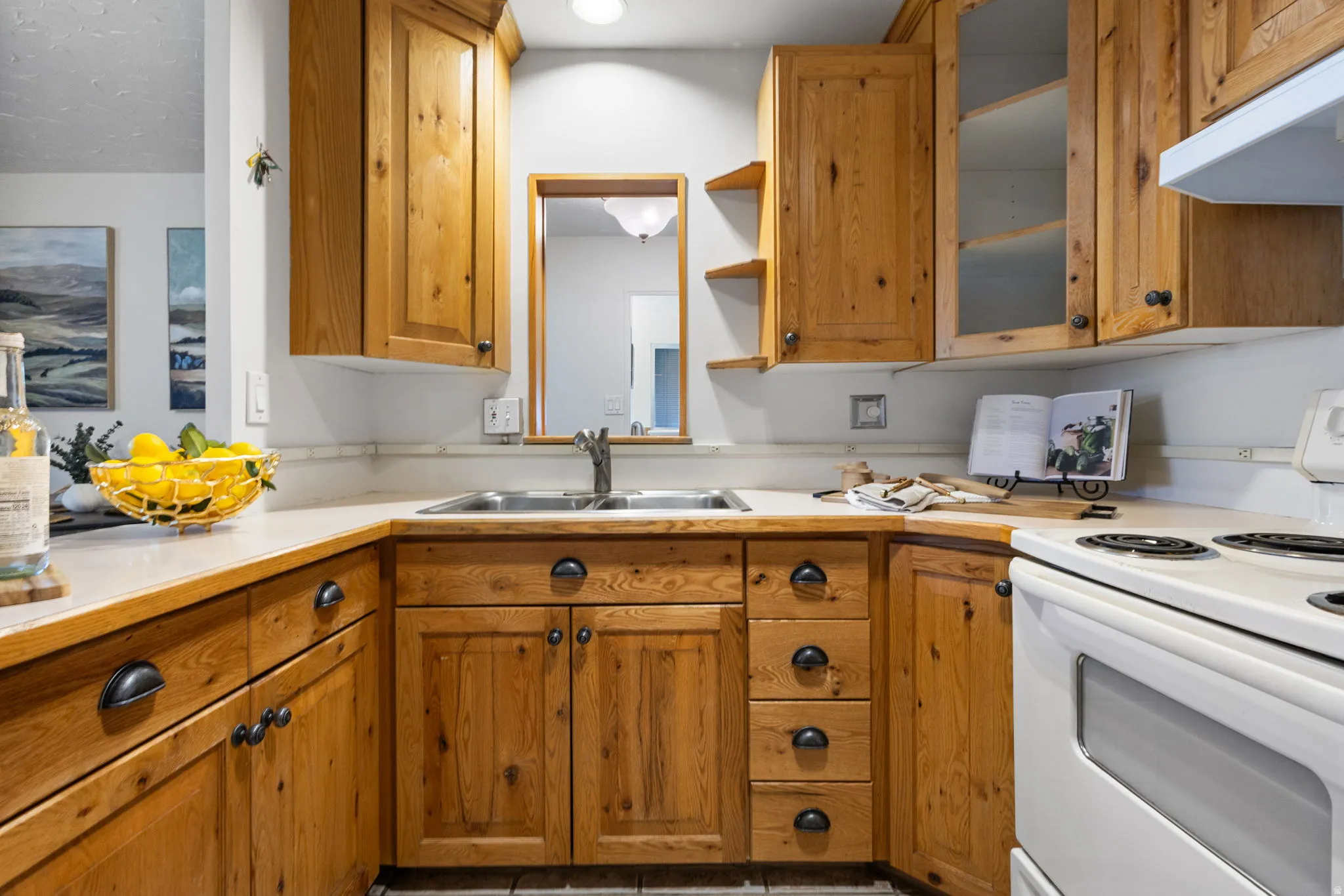 Kitchen showcasing wood cabinetry, a double basin sink with a single-lever faucet, light-toned countertops, and a white electric range