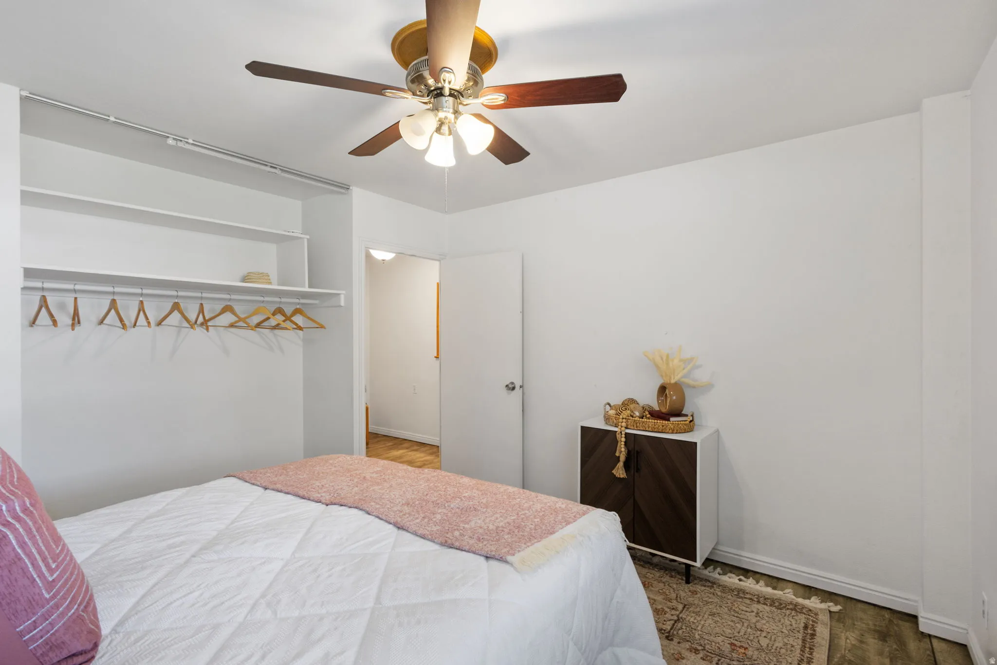 Bedroom featuring a ceiling fan with integrated lighting, open shelving closet system, and wood-finish flooring