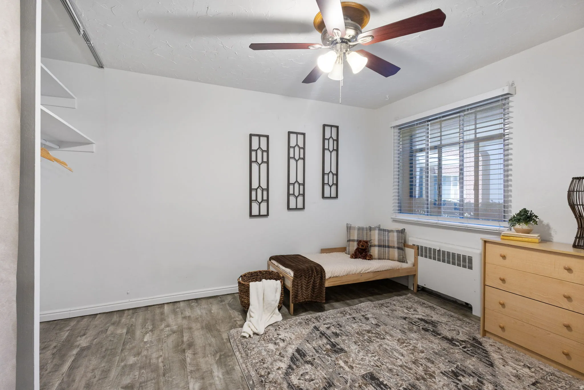 Second bedroom featuring a window with horizontal blinds, a ceiling fan with light fixture, and wood-finish flooring