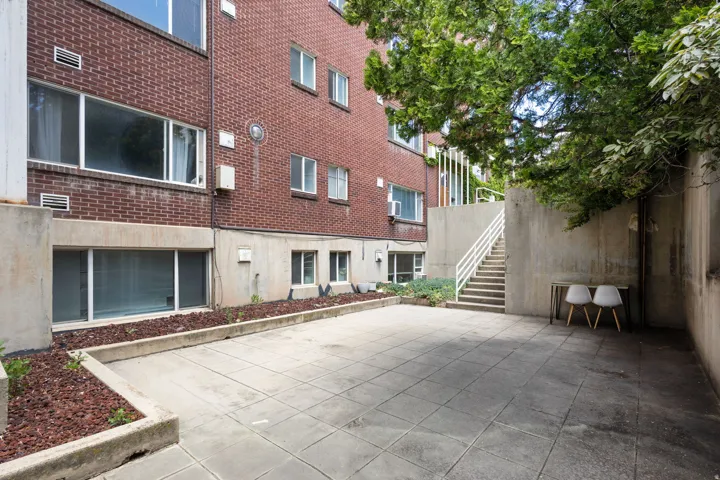 Expansive patio area featuring large concrete pavers, concrete retaining walls, and a brick exterior building