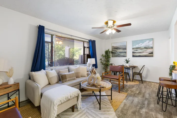 Living area featuring wood-finish flooring, a ceiling fan with integrated lighting and a large window