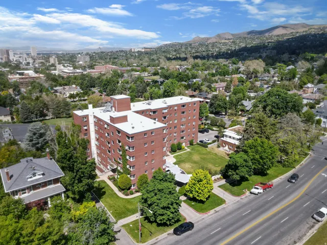 Red brick multi-story building featuring multiple windows, a white flat roof, and a surrounding green lawn