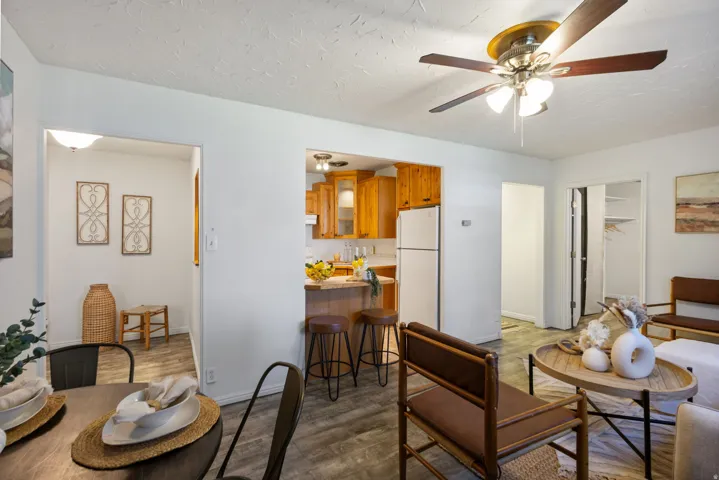 Living area with wood-finish flooring, a ceiling fan, and a kitchen featuring wood cabinetry and white appliances