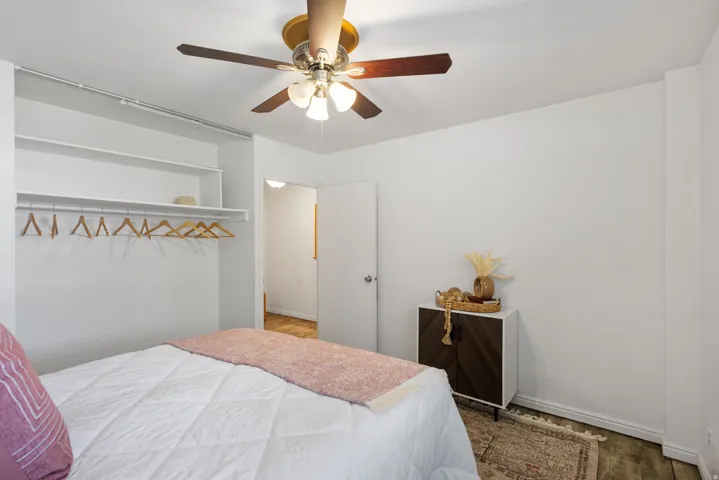 Bedroom featuring a ceiling fan with integrated lighting, open shelving closet system, and wood-finish flooring