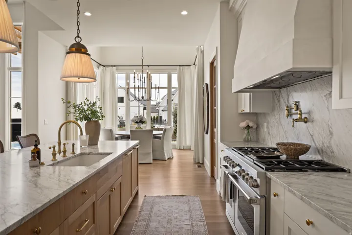 Gourmet kitchen featuring a large central island with an integrated sink, professional-grade range, full-height stone slab backsplash, and wood-finish flooring