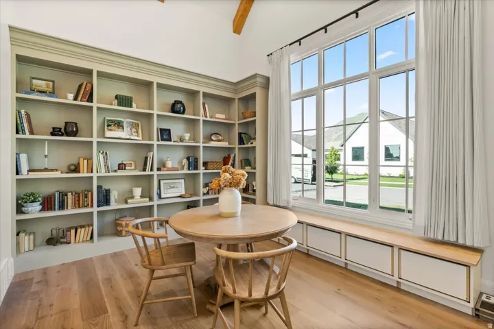 Spacious room featuring extensive built-in shelving, large multi-pane windows, wood-finish flooring, a vaulted ceiling with exposed beam, and integrated window seating with storage