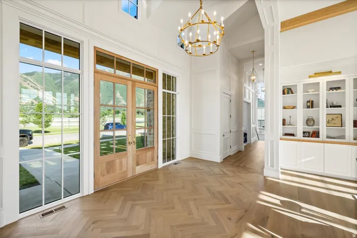Grand entryway featuring double-door entry with transom windows, herringbone wood-finish flooring, and a large brass chandelier