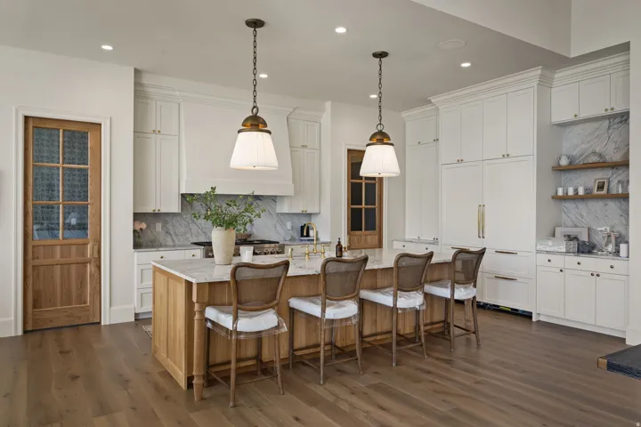 Gourmet kitchen featuring a wood-finish island with seating, integrated paneled appliances, marble countertops and backsplash, white cabinetry, and wood-finish flooring