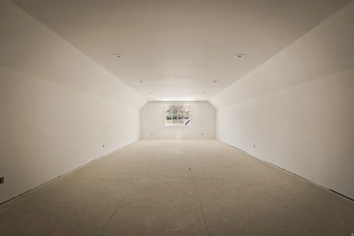 Spacious attic room featuring white walls, vaulted ceilings, recessed lighting, and a double window