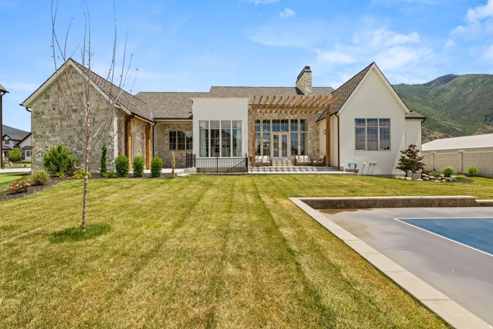 Expansive rear exterior featuring a stone and stucco facade, a pergola-covered patio, and a dedicated sport court